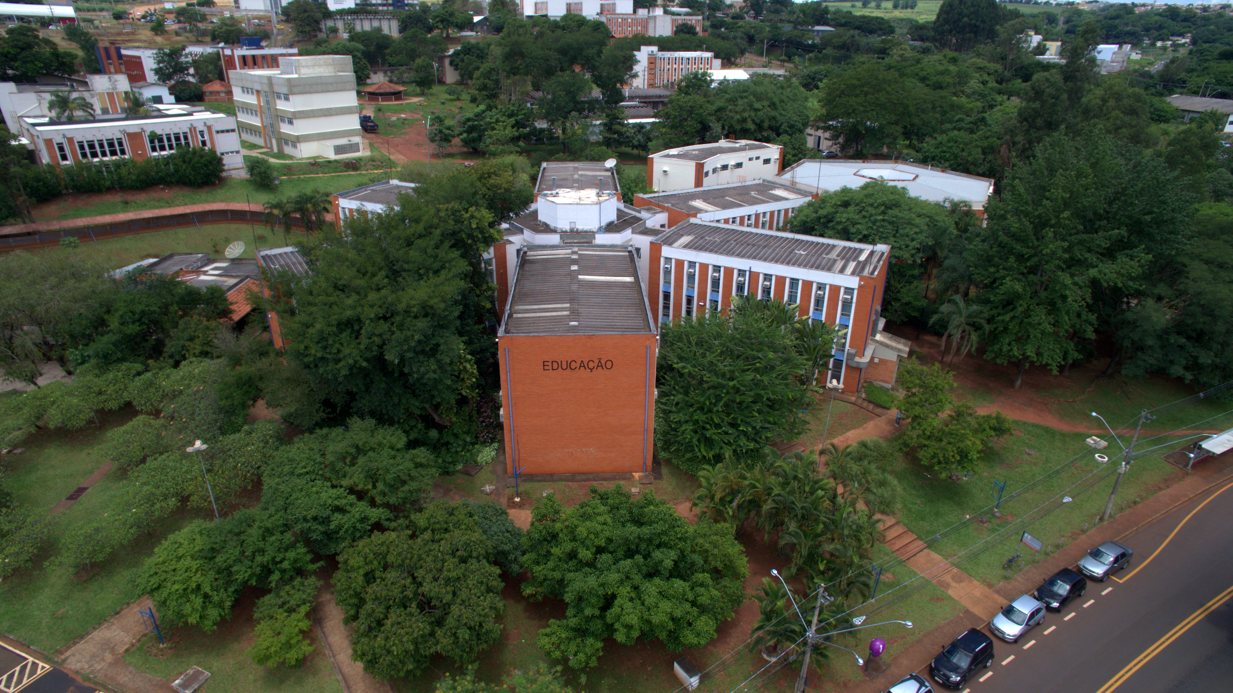 Fotografia aérea do prédio Paulo Freire da Faculdade de Educação. O prédio possui arquitetura em formatod e asterisco, com paredes altas de tijolos marrons nas pontas, em meio a grandes árvores.