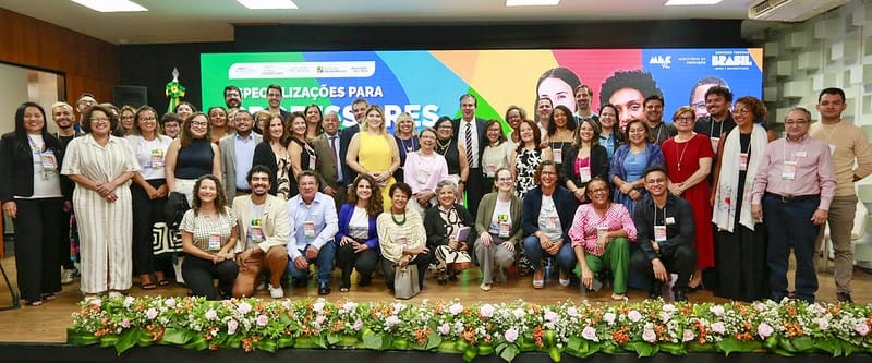 Uma grande quantidade de pessoas reunida em um evento, sobre um palco, com imagens projetadas no fundo.