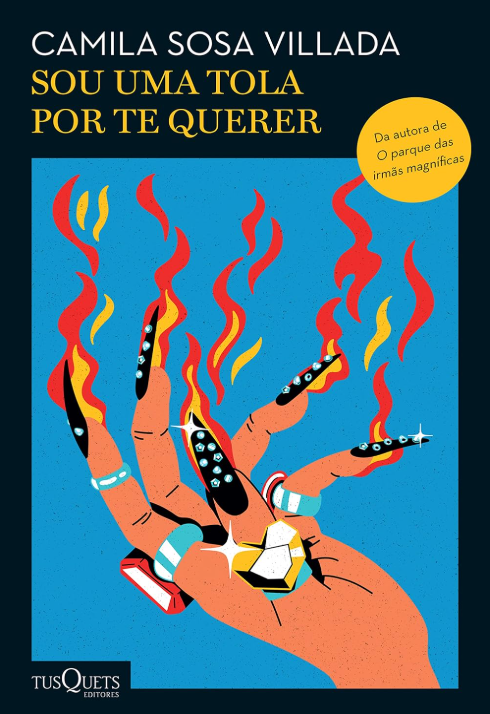 Capa do livro "Sou uma tola por te querer", composta por um fundo azul com um desenho estilizado de uma mão parcialmente dobrada, com unhas compridas e afiadas, pintadas de preto, com chamas saindo de cada dedo, ornados com vários anéis coloridos. Em uma borda preta, aparecem o título do livro, o nome da autora e da editora.