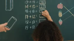 Criança escrevendo resultados de operações matemáticas com um giz em uma lousa.
