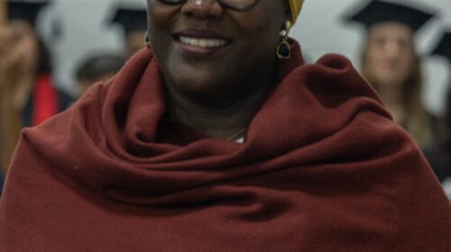 Mulher negra usa vestes brancas, lenço terracota e turbante branco.