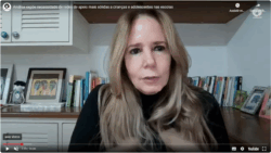 Captura de tela de computador que mostra vídeo no YouTube. No vídeo, há uma mulher sentada em um local parcialmente iluminado, o fundo é uma parede com estantes e livros. A mulher é branca, tem cabelo liso, longo e loiro e veste roupa preta. Fim da descrição.