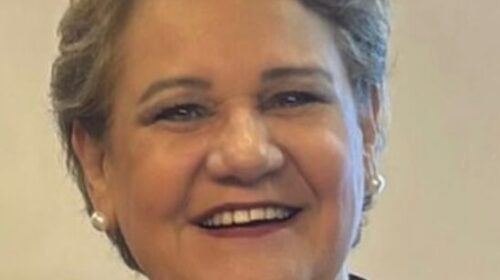 Fotografia que mostra a professora Ana Aragão, da Faculdade de Educação da Unicamp. Ana é uma mulher branca, com cabelo curto e grisalho. Ela sorri e veste uma roupa colorida, um colar de pedras grandes e brincos de pérola. Fim da descrição.