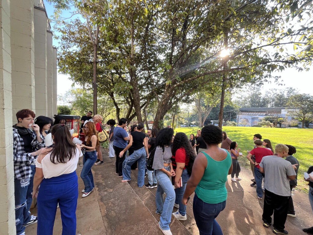 Fotografia que mostra vários estudantes reunidos em área externa da FE. Fim da descrição.