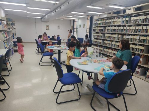 Foto de um espaço em uma biblioteca com instrutores e crianças