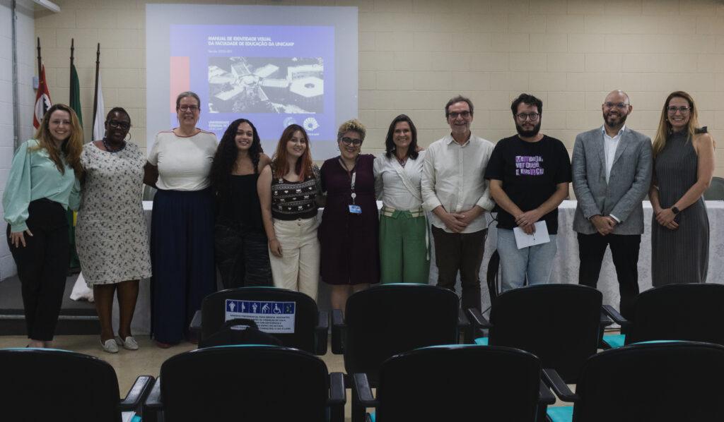 Fotografia que mostra um grupo de 11 pessoas sorrindo e posando para a câmera. O ambiente é uma sala fechada e bem iluminada e há cadeiras, mesa, bandeiras no ambiente. As pessoas vestem roupas formais. Fim da descrição.