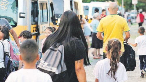 Fotografia que mostra crianças e responsáveis andando em direção a vans escolares. Fim da descrição.